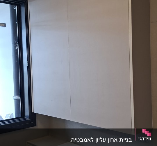 ארון שירות מעוצב בחדר רחצה מעל חלון ושירותים